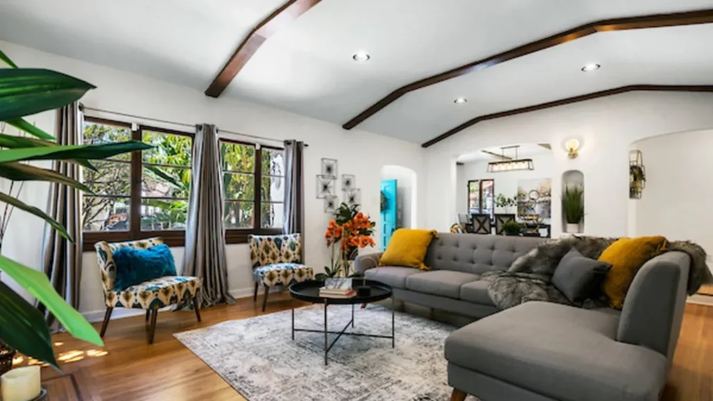 Living room with a gray sectional, yellow pillows and dark ceiling beams