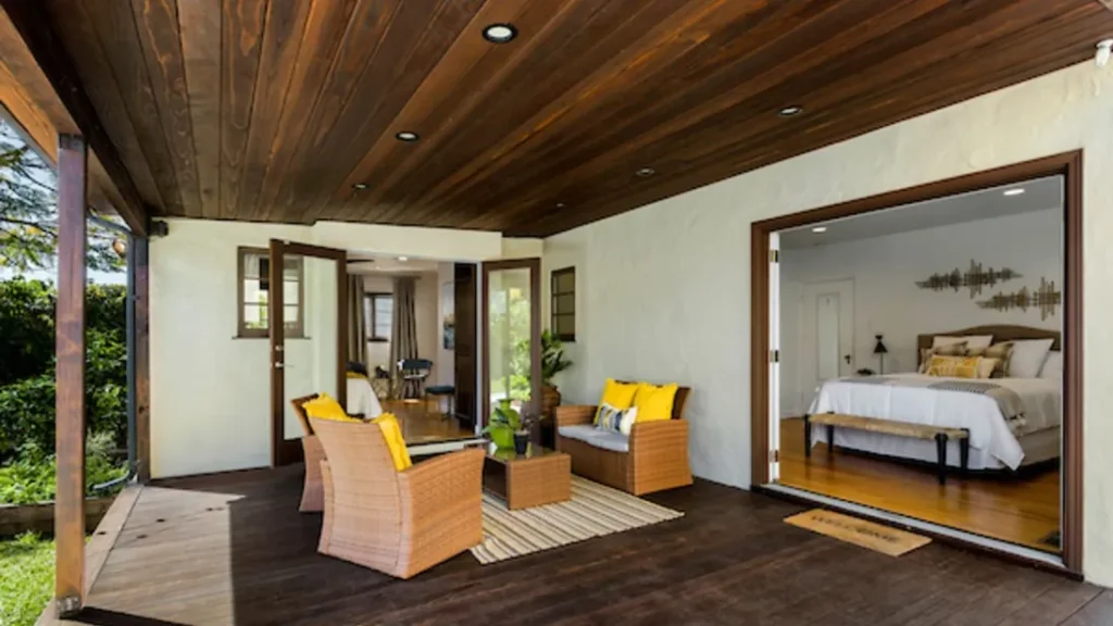 Covered patio with wicker chairs, yellow pillows and a wood ceiling outside the bedroom