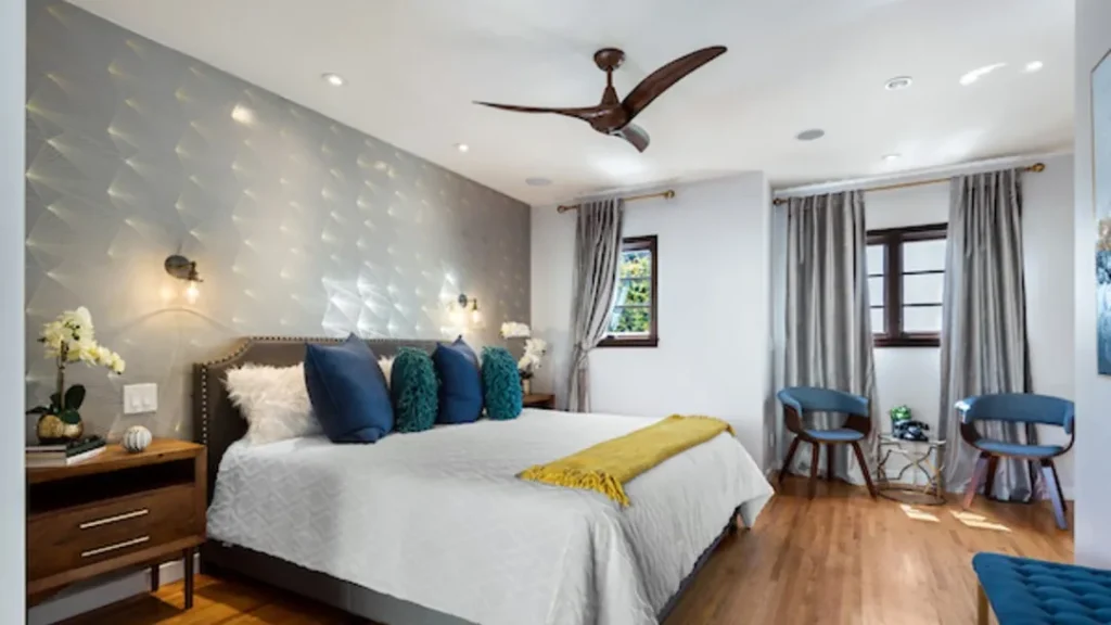 Bedroom with gray patterned wallpaper, teal pillows and two blue chairs