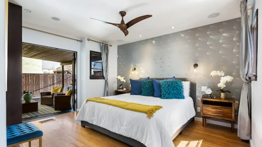 Bedroom with gray accent wallpaper, teal pillows and a patio door