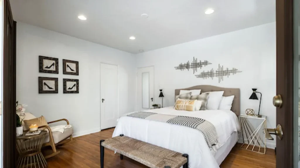Bedroom with a beige headboard, white bedding, a bench and framed bird prints