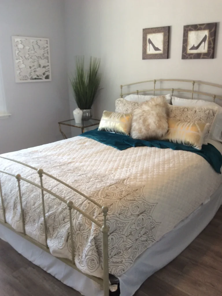 Bedroom with a brass bed frame, white bedding and teal accents