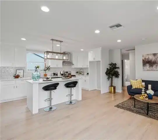White kitchen with an island, black stools and a navy sofa in the living area