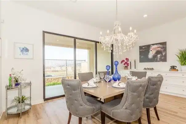 Dining room with gray tufted chairs, a crystal chandelier and a sliding door view