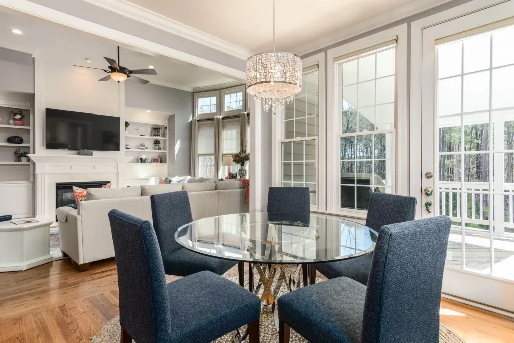 Dining area with a round glass table, navy chairs and a crystal chandelier