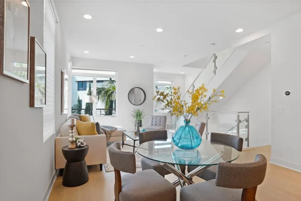 Dining area with a round glass table, gray chairs and a yellow flower arrangement