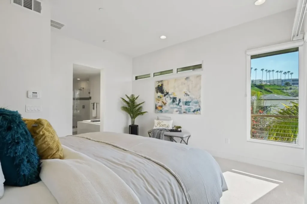 Bedroom with white bedding, teal and yellow pillows and large windows
