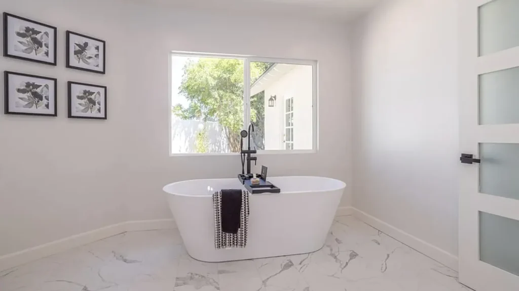 Bathroom with a freestanding white tub, black floor faucet and marble floors