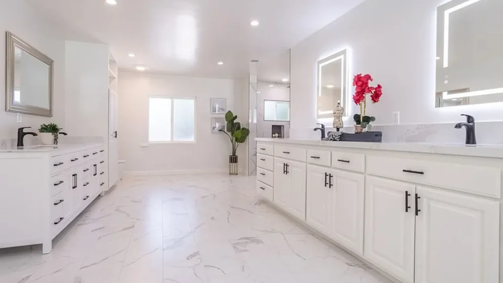 Bathroom with a long white double vanity, lighted mirrors and marble floors