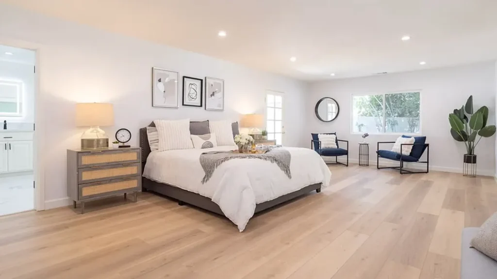Bedroom with white bedding, framed art above the bed and two accent chairs
