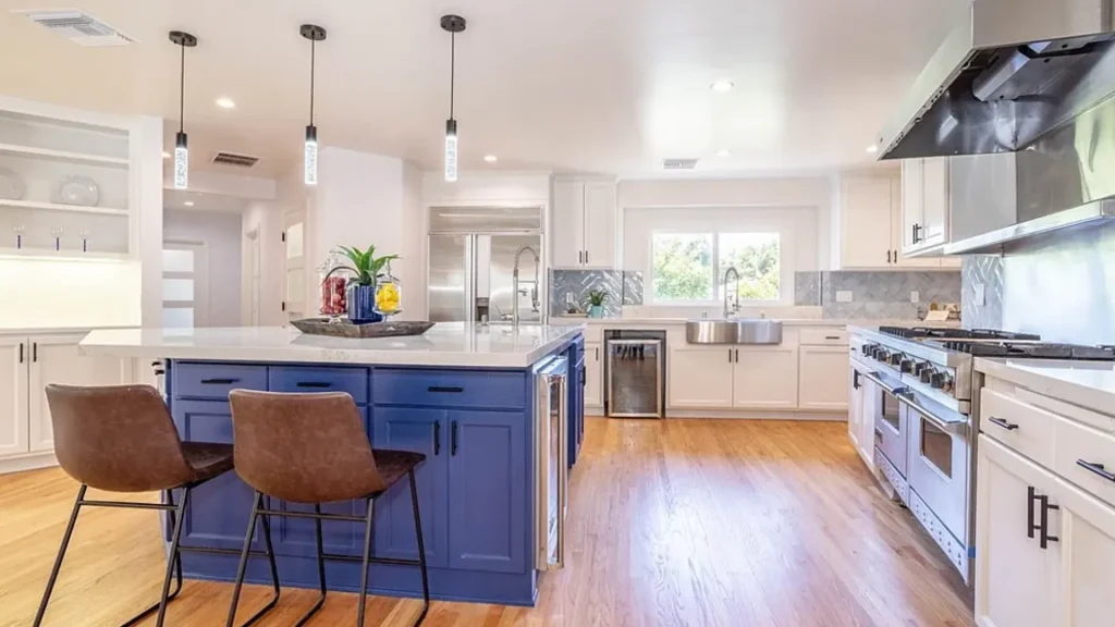 Open kitchen with a blue island, brown leather stools and pendant lights