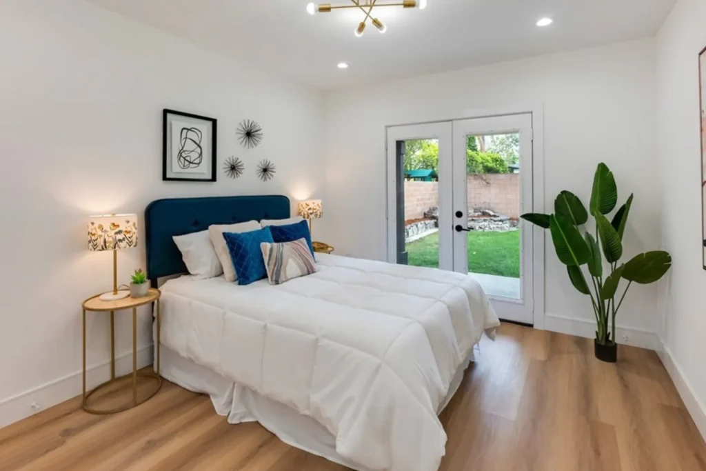 Bedroom with a teal velvet headboard, white bedding and French doors to the yard