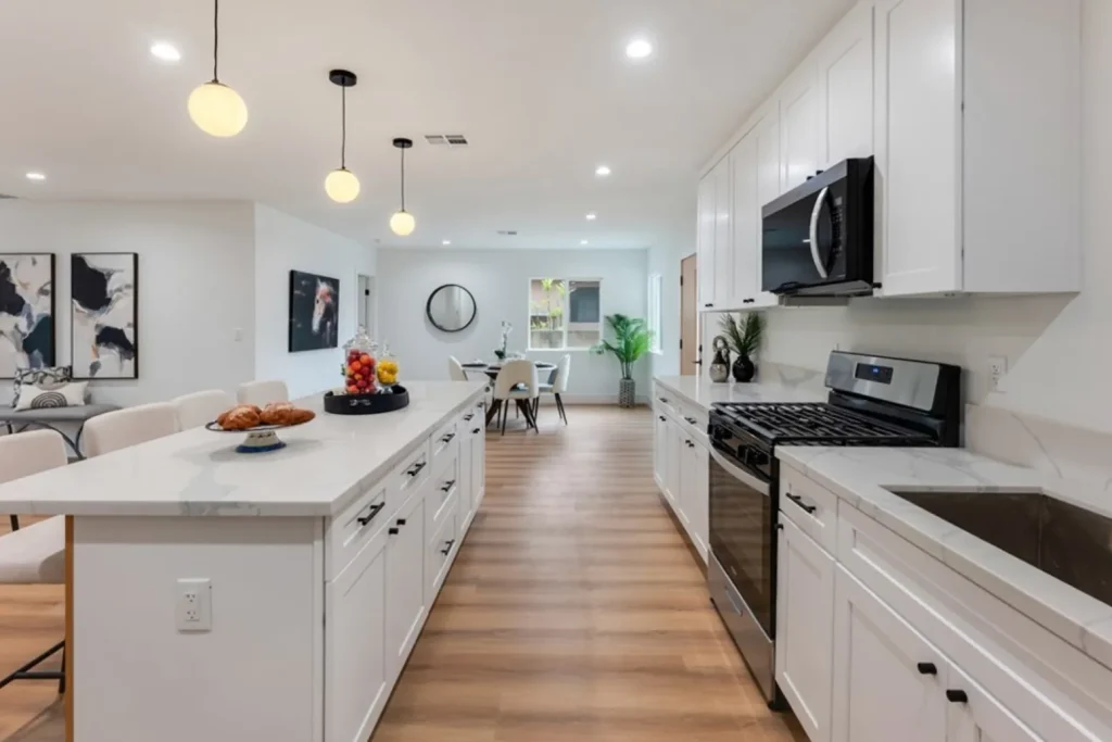 Long white kitchen with a marble island, pendant lights and stainless appliances