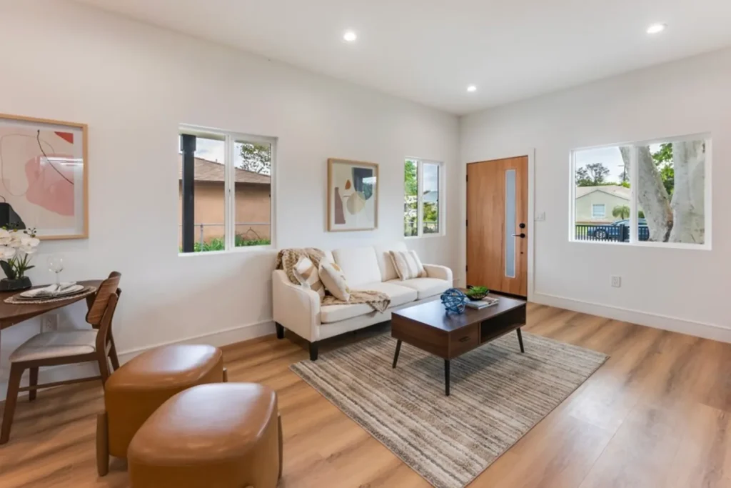 Living room with a cream loveseat, leather ottomans and a small dining table