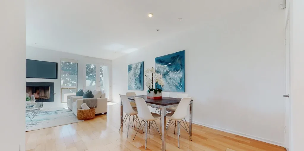 Open dining area with a white table and chairs beside a living room with a fireplace