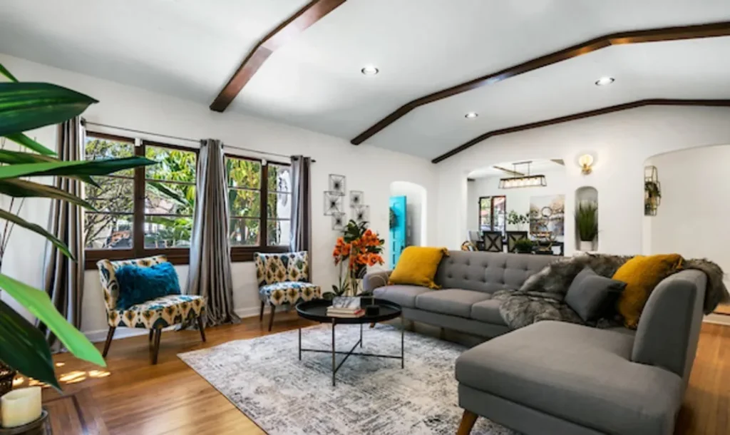 Living room with a gray sectional, yellow and blue pillows and a beamed ceiling