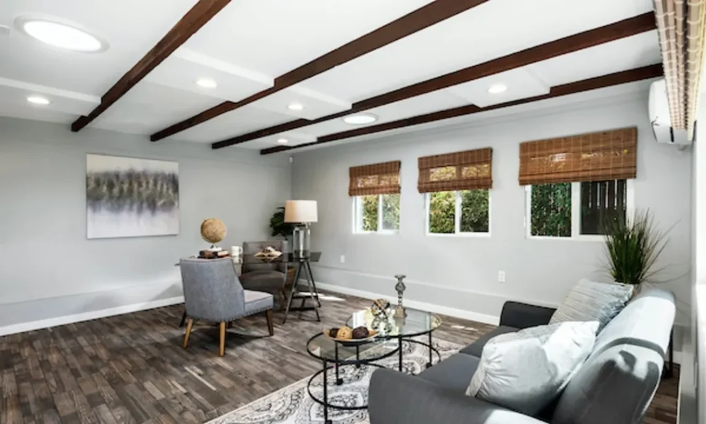 Living room with gray sofas, a patterned rug and dark wood ceiling beams
