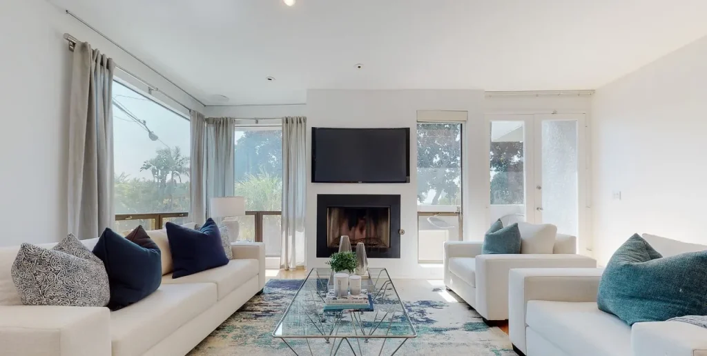 Living room with a white sectional, blue accents and a glass coffee table by the fireplace